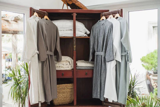 A wooden closet with linen robes hanging inside.