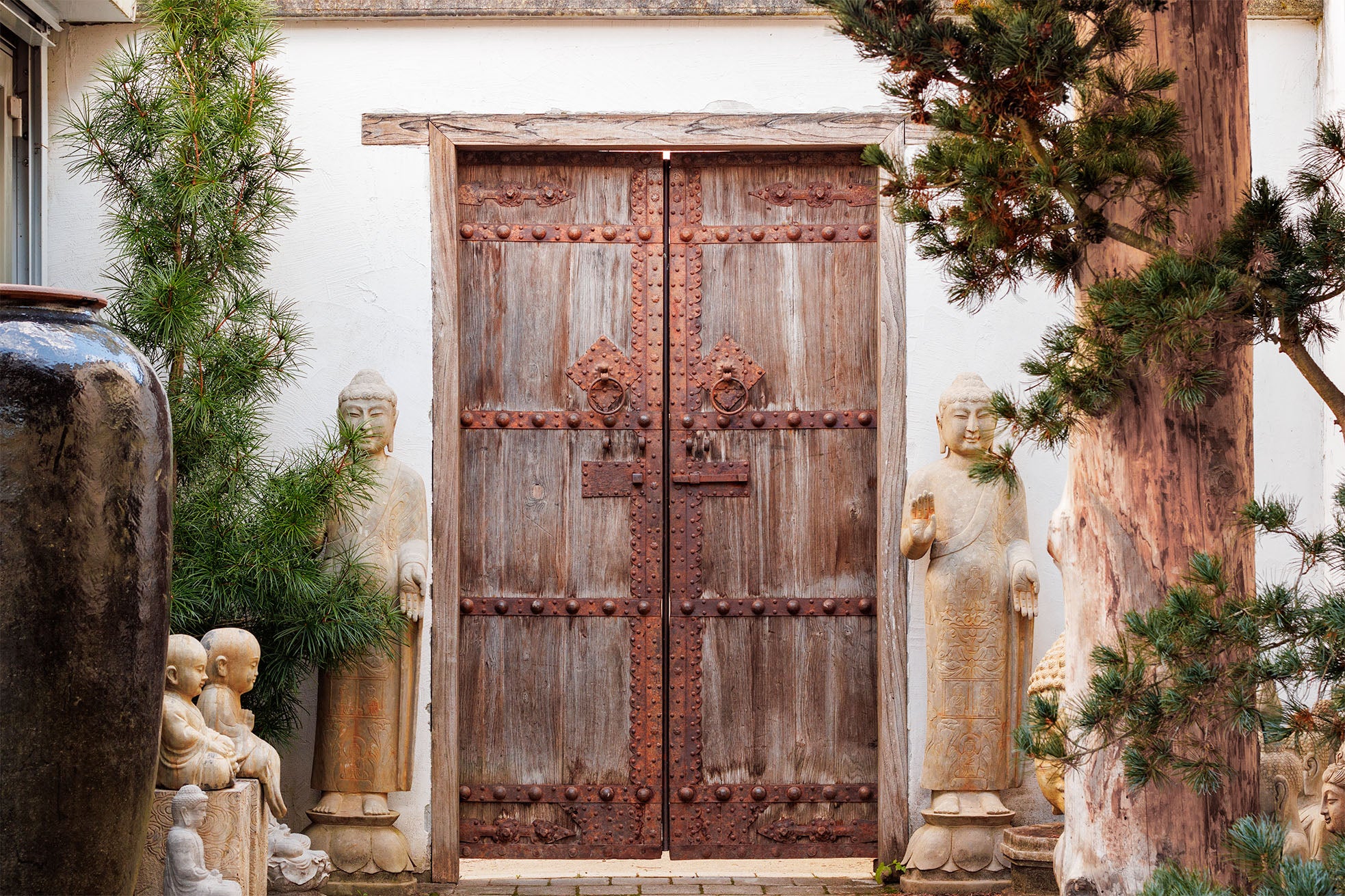 Wooden double doors with decorative elements in a garden setting with statues and plants.